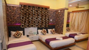 A hotel room with three beds, a wooden headboard, a patterned curtain, and a brown rug. - Hotel Royal Inn By Glitz (Mangaluru)