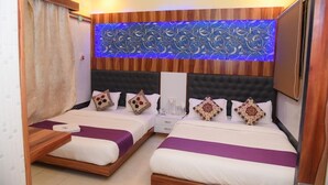 A hotel room with two beds, a decorative wall panel, a ceiling light, and a window with blinds. - Hotel Royal Inn By Glitz (Mangaluru)