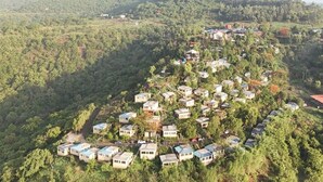 A cluster of small, uniformly designed buildings with flat roofs, surrounded by dense greenery and hilly terrain. - Mantra Resort Pvt Ltd (Bhor)