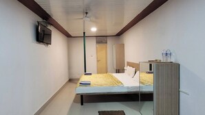 A narrow hotel room with a bed, a television, a water bottle, and a mirror. - Mantra Resort Pvt Ltd (Bhor)