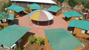 A courtyard with multiple buildings, each with a green roof and a central structure featuring a colorful umbrella. - Mantra Resort Pvt Ltd (Bhor)