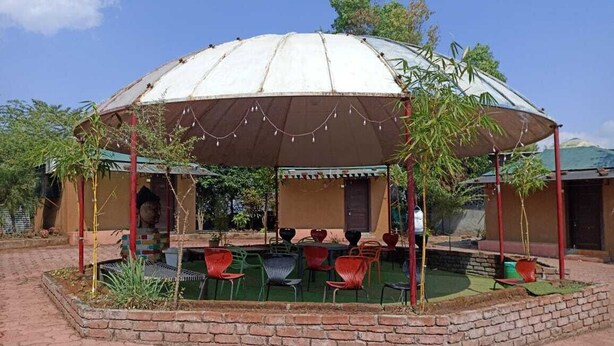 A covered outdoor seating area with chairs and tables, surrounded by a brick wall and greenery. - Mantra Resort Pvt Ltd (Bhor)