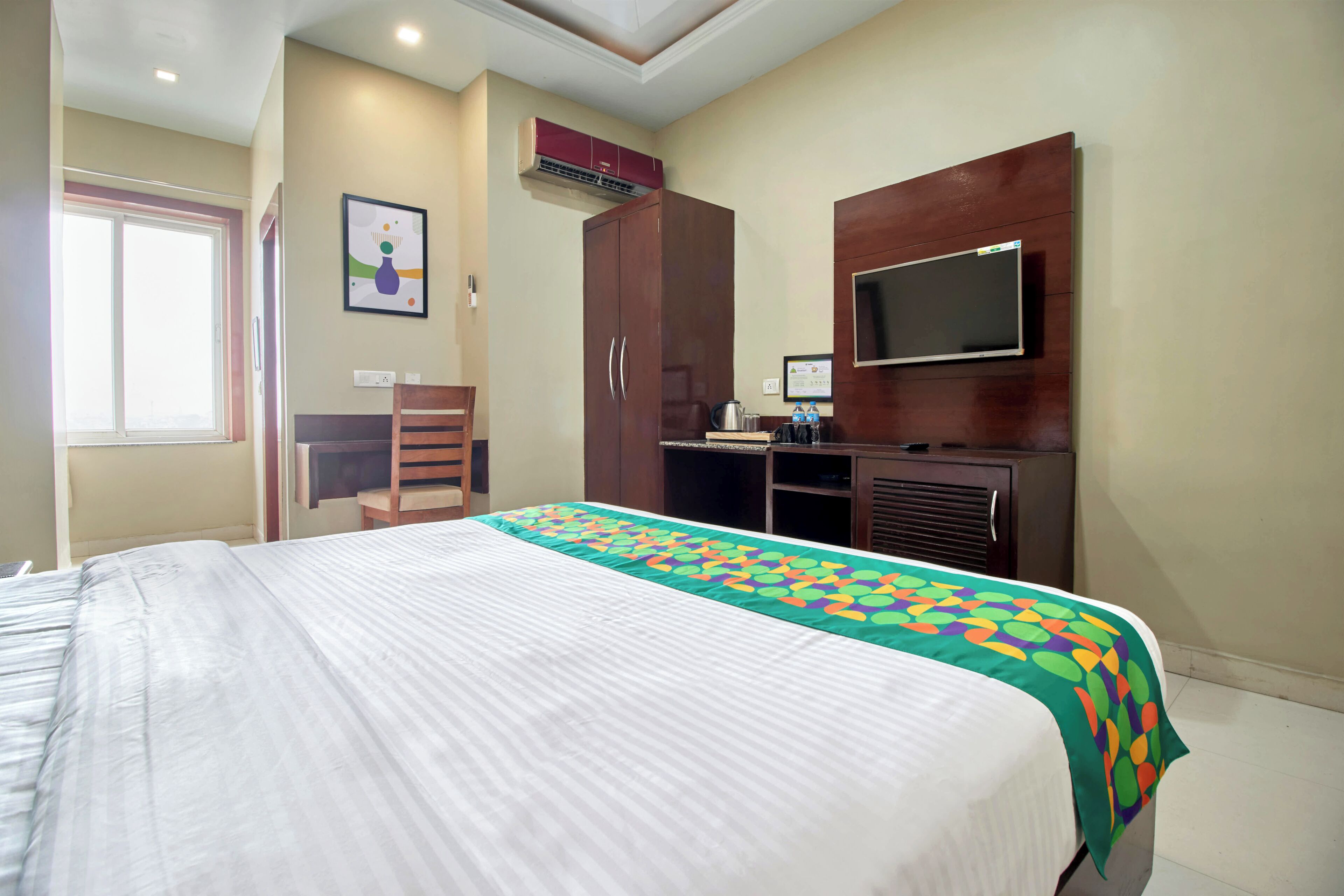 Quarto de hotel com cama, escrivaninha, cadeira, televisão e ar condicionado.