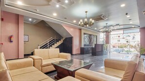 Un hall d’entrée avec des canapés de couleur beige, une table basse en verre, un lustre, un escalier et un extincteur.