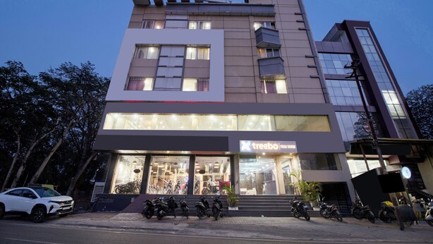 Un immeuble à plusieurs étages avec une devanture portant l’inscription « Treebo » et plusieurs motos garées devant.