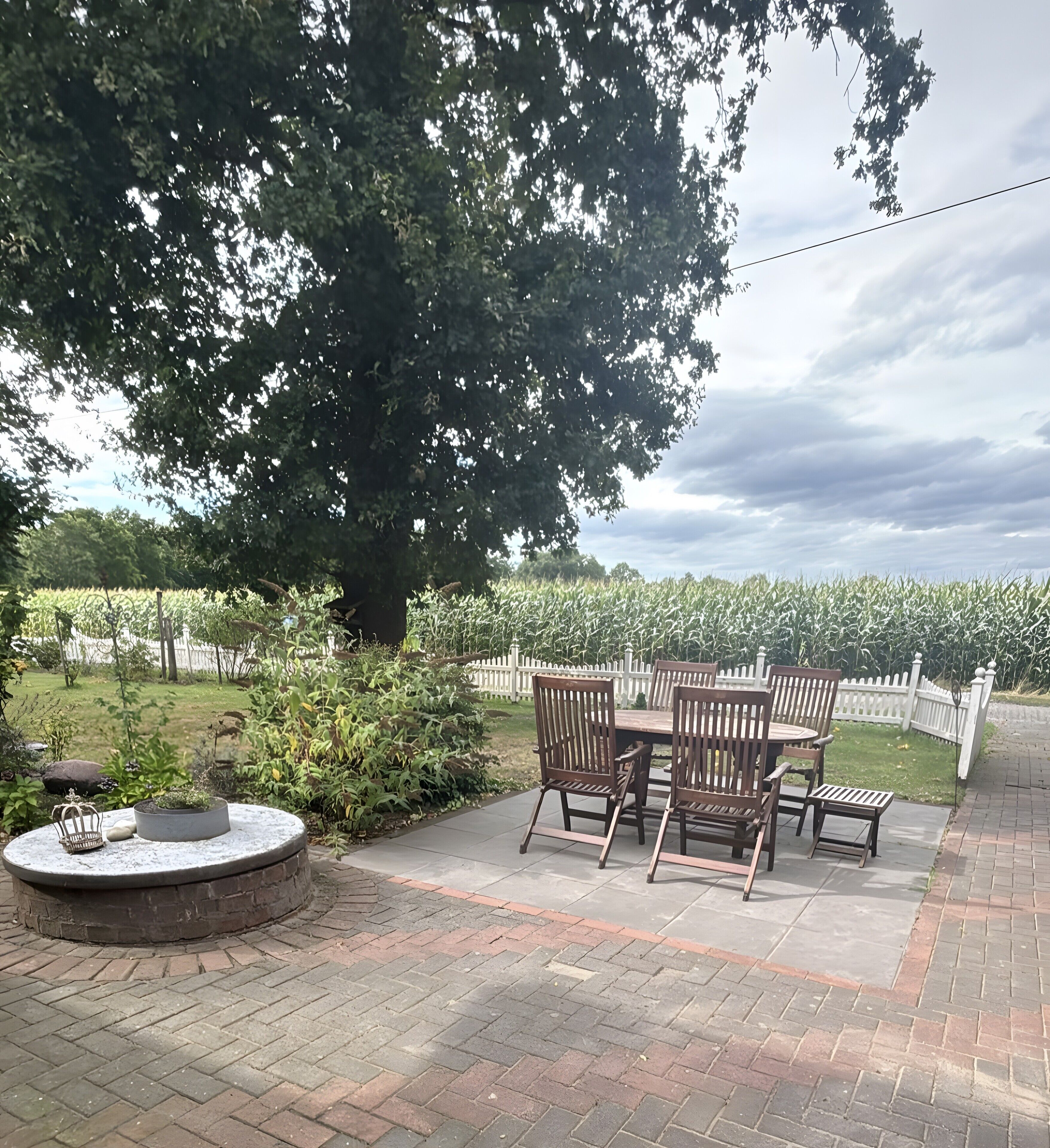 A patio with a table and chairs, surrounded by a brick pathway and a garden.
