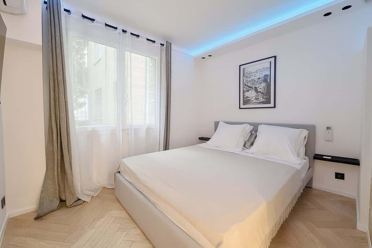 A bedroom with a bed, curtains, a wall-mounted light, and a framed picture.