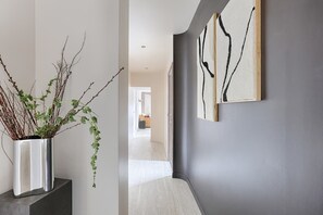 A hallway with a potted plant, a dark wall with abstract art, and a view into another room. - Appartement de luxe vue sur la Madeleine (Paris)