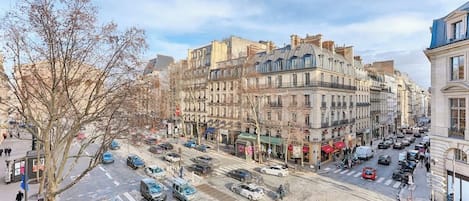 A city street with parked cars, buildings, and a tree.