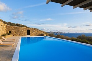 A pool with a view of the sea and mountains, stone walls, and lounge chairs. - Apartment Semi-private Huge Pool (Mykonos)