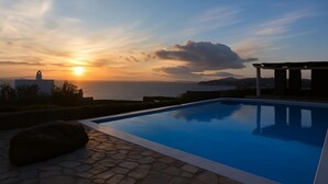 Una piscina con vista sul tramonto, pavimento in pietra e struttura a pergola.