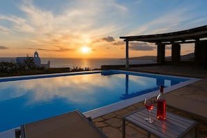 A swimming pool with a sunset view, a pergola, and a table with a bottle and glass. - Apartment Semi-private Huge Pool (Mykonos)