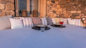 Un muro di pietra, una finestra con un cesto, un tavolo con un bicchiere di vino rosso e un cuscino con cuscini a righe.