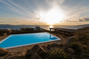 A swimming pool with a sunset view, stone pathway, and outdoor seating area. - Apartment Semi-private Huge Pool (Mykonos)