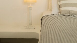Un letto con una coperta a righe, una lampada da comodino e dei cuscini appoggiati a una parete strutturata.