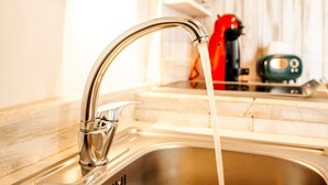 Ein Edelstahl-Spülbecken mit fließendem Wasser, ein roter Wasserkocher und ein grünes Gerät auf der Arbeitsplatte.
