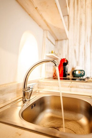 Ein Edelstahl-Spülbecken mit fließendem Wasser, ein roter Wasserkocher und ein grünes Gerät auf der Arbeitsplatte.