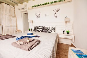 A bedroom with a bed, a bedside table, a nightstand, a wall-mounted shelf with greenery, and artwork depicting hands holding. - Opus Studio by Mykonian Hospitality (Mykonos)