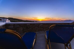 A terrace with stone walls, two blue chairs, and a sunset view. - Opus Apartment by Mykonian Hospitality (Mykonos)
