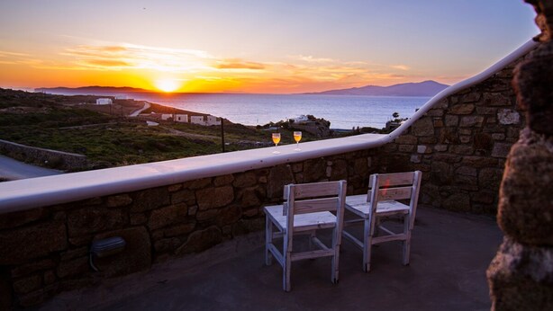 A terrace with stone walls, two white chairs, and a sunset view over the sea. - Opus Apartment by Mykonian Hospitality (Mykonos)