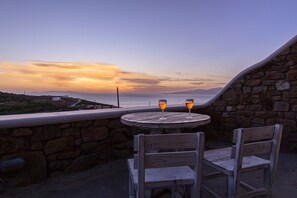 A stone wall, a round wooden table with two chairs, and two glasses of orange liquid. - Opus Apartment by Mykonian Hospitality (Mykonos)