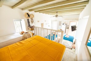 A bedroom with a bed, a window, a ceiling fan, and a view of the kitchen. - Opus Apartment by Mykonian Hospitality (Mykonos)