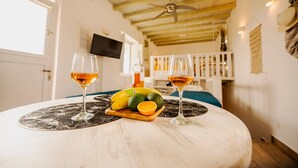 A room with a round table, two glasses of wine, a fruit bowl with bananas and an orange, and a TV mounted on the wall. - Opus Apartment by Mykonian Hospitality (Mykonos)