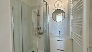 Un baño moderno con ducha de vidrio, lavamanos blanco con espejo y un perchero para toallas.