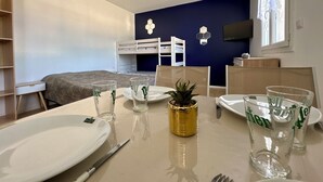 Una habitación con una cama nido, una mesa de comedor con platos y vasos, una planta pequeña y un televisor en la pared.