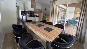 Ett modernt kök med vita skåp, ett matbord med svarta stolar och utsikt över omgivningen genom en skjutdörr i glas.