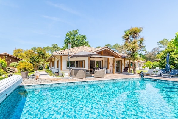 A poolside area with a house, outdoor furniture, and a clear blue pool.