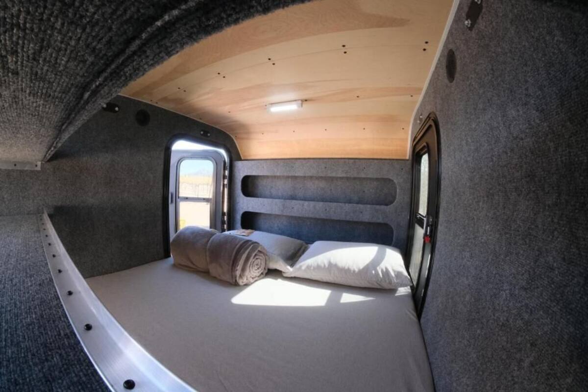 A compact, well-lit interior with a bed, a window, and a door.