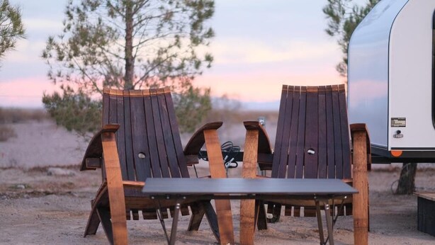 Two Adirondack chairs with a metal table in a sandy outdoor setting. - Tarantula Ranch Vineyard - Death Valley (Amargosa Valley)