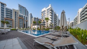 A rooftop pool area with lounge chairs, a swimming pool, and modern high-rise buildings in the background. - Free Housekeeping Visits During Your Stay - Stayshort - Peaceful Studio for 2 in Meydan (Dubai)