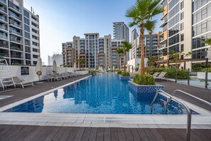 Ein Swimmingpool mit Liegestühlen und Palmen, umgeben von modernen Wohngebäuden.