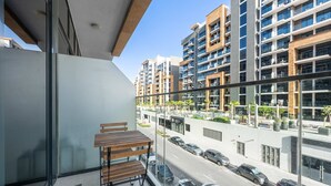 A balcony with a table and chairs, overlooking a street with cars and modern buildings. - Free Housekeeping Visits During Your Stay - Stayshort - Peaceful Studio for 2 in Meydan (Dubai)