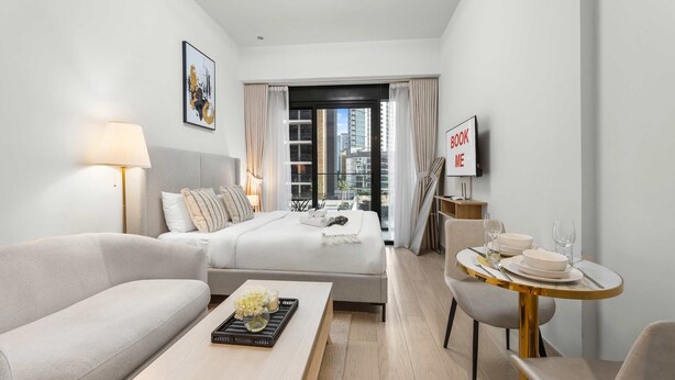 A modern hotel room with a bed, a sofa, a dining table with chairs, a lamp, and a view of the cityscape. - Free Housekeeping Visits During Your Stay - Stayshort - Peaceful Studio for 2 in Meydan (Dubai)