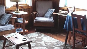 Een gezellige kamer met houten wanden, een grijze fauteuil, een klein tafeltje met een lamp en een blauwe tafelkleed.
