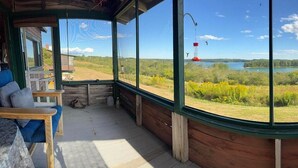 A room with a large window overlooking a lake and forest, wooden walls, a bench, and a hanging bird feeder.