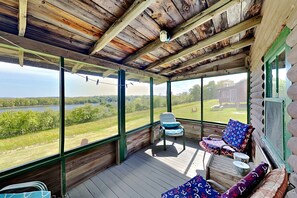 A covered porch with a view of a lake, wooden walls, and a chair with patterned cushions. - Family-Friendly Castine Escape | Games, Kayaks & Views (Castine)