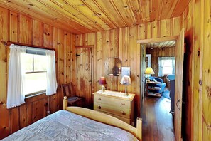 A wooden cabin bedroom with a bed, dresser, mirror, and a view into the living area. - Family-Friendly Castine Escape | Games, Kayaks & Views (Castine)