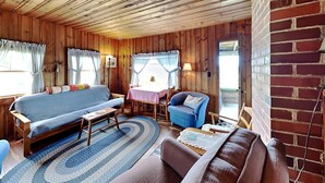 Interior de una cabaña de madera con sofá, sillón y mesa de comedor.