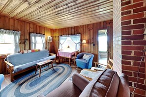 A wooden cabin interior with a sofa, armchair, and dining table. - Family-Friendly Castine Escape | Games, Kayaks & Views (Castine)