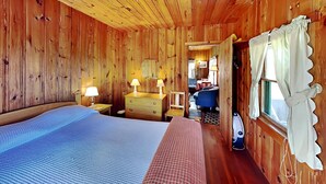Una habitación de cabaña de madera con dos camas, un aparador, un espejo y una ventana con cortinas.