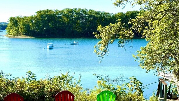 Dos sillas Adirondack mirando un lago con barcos, rodeado de árboles y un muelle.
