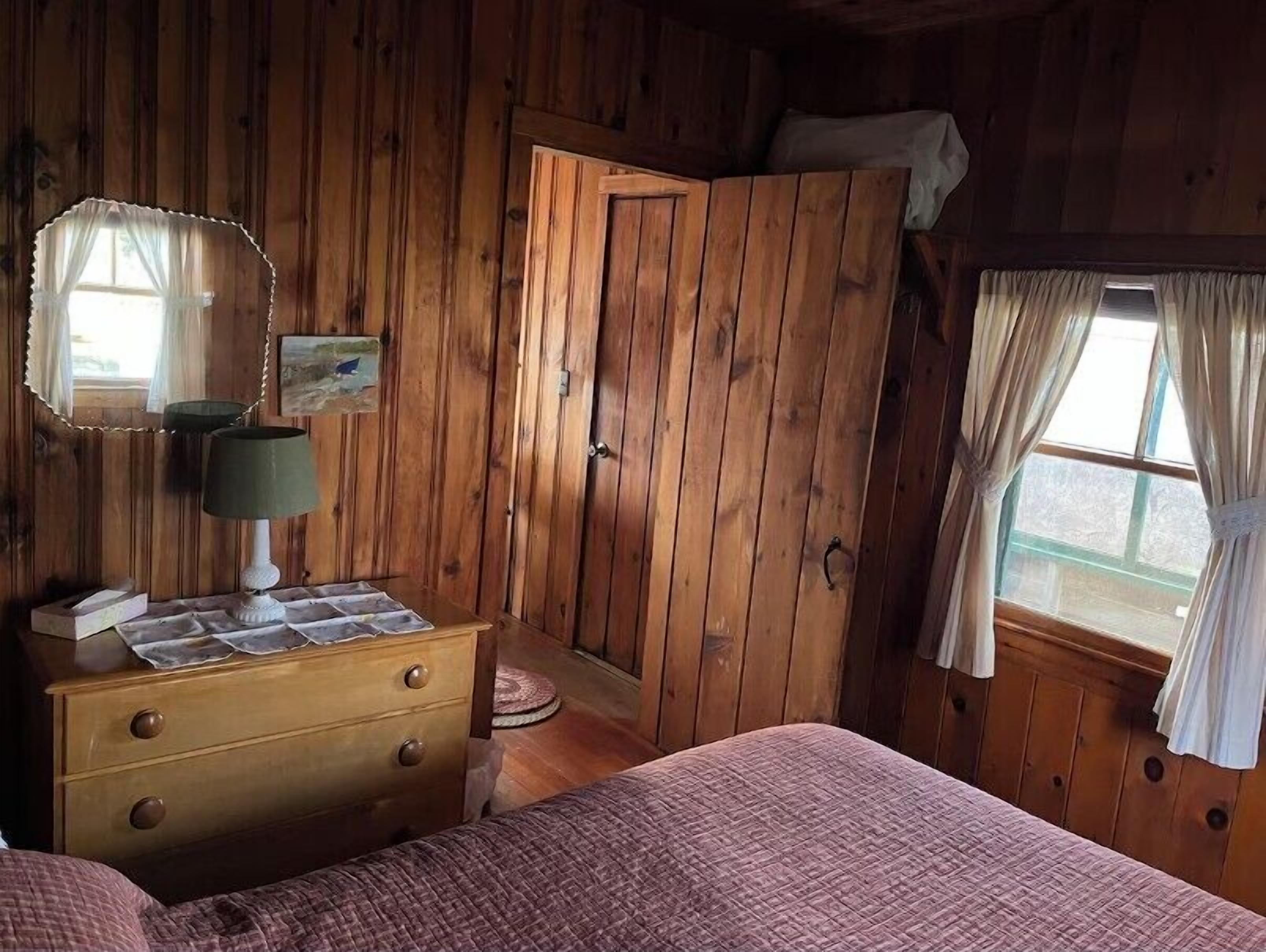 Une chambre dans une cabane en bois, avec un lit, une commode, un miroir et une porte.