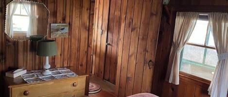 Une chambre dans une cabane en bois, avec un lit, une commode, un miroir et une porte.