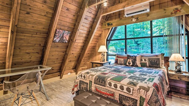 Un dormitorio de cabaña de madera con una cama, una mesa de vidrio transparente y un ventanal grande.