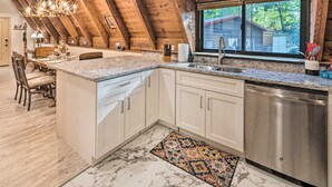 Una cocina con encimera de granito, armarios blancos, lavavajillas de acero inoxidable y techo de madera.