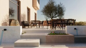 Un área de estar exterior moderna con sillas y mesas, un árbol pequeño y una fuente de agua.